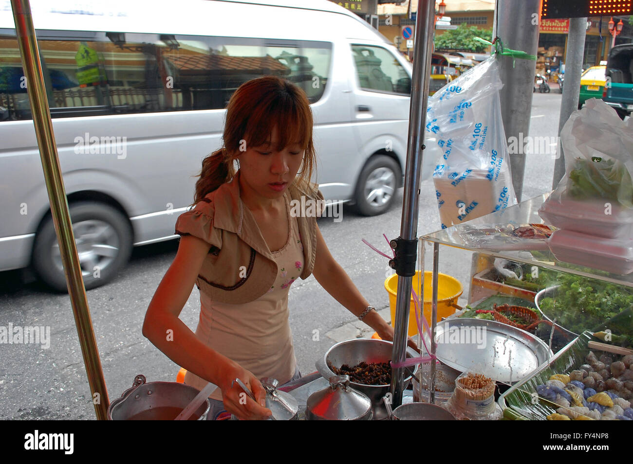 Cucina di strada venditore prepara i suoi piatti come il traffico ruggisce da a Bangkok, in Thailandia Foto Stock