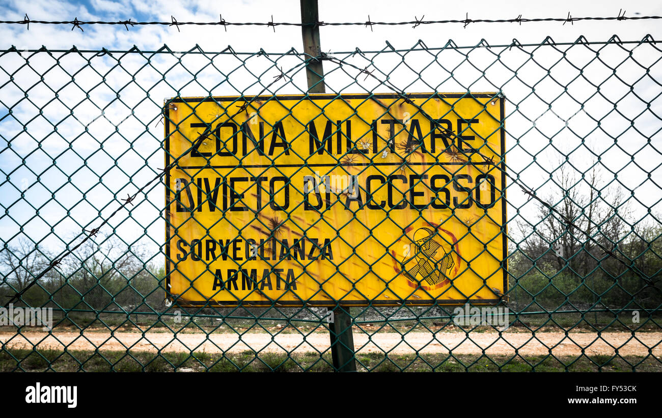 Cartello giallo che legge in italiano "militare zona, nessuna voce, sorveglianza armata'. Foto Stock