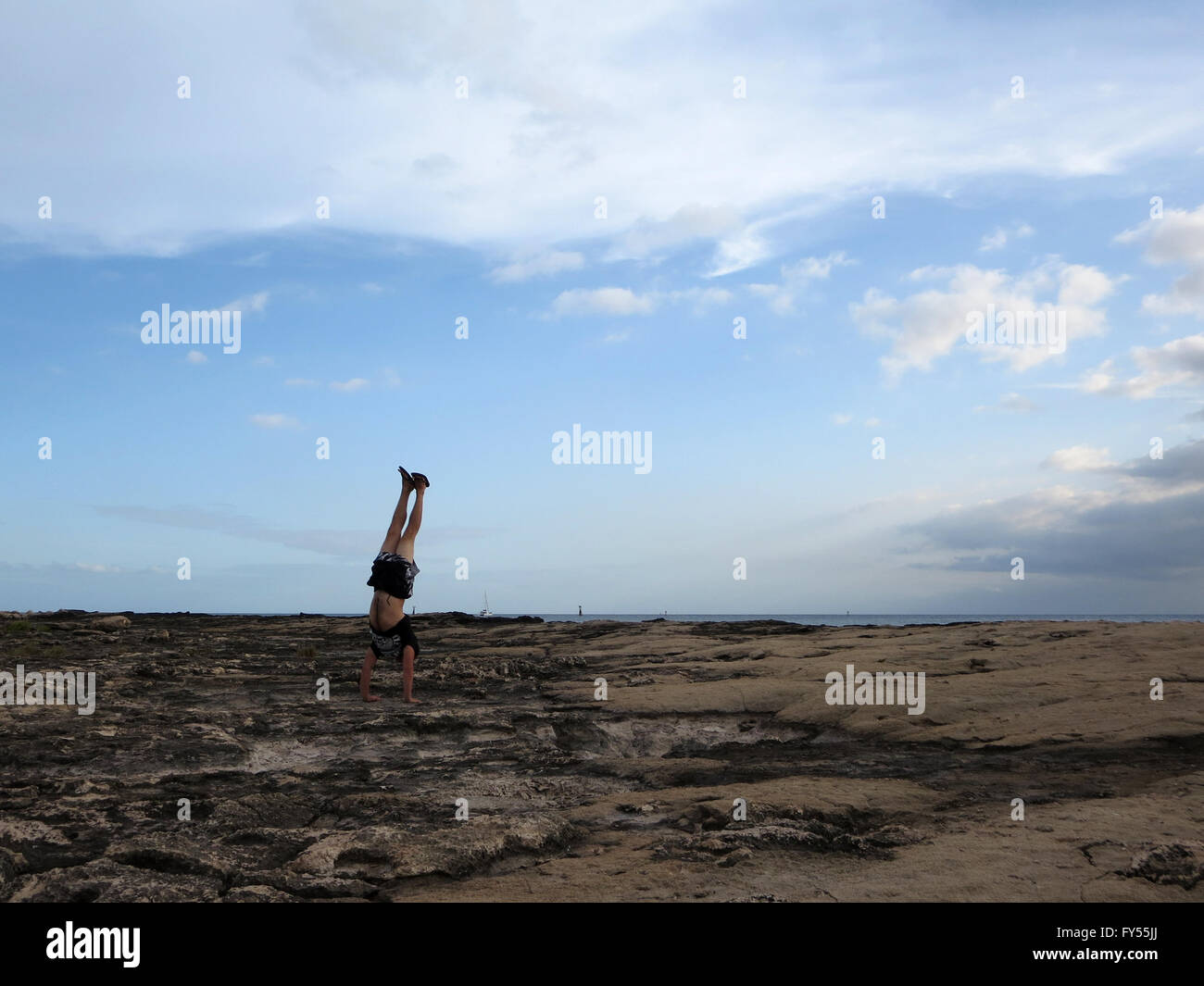 L'uomo indossare una t-shirt, corti e pantofole le verticali sulla riva rocce di Ko Olina su Oahu, Hawaii con drammatica nuvole, cielo, e Foto Stock