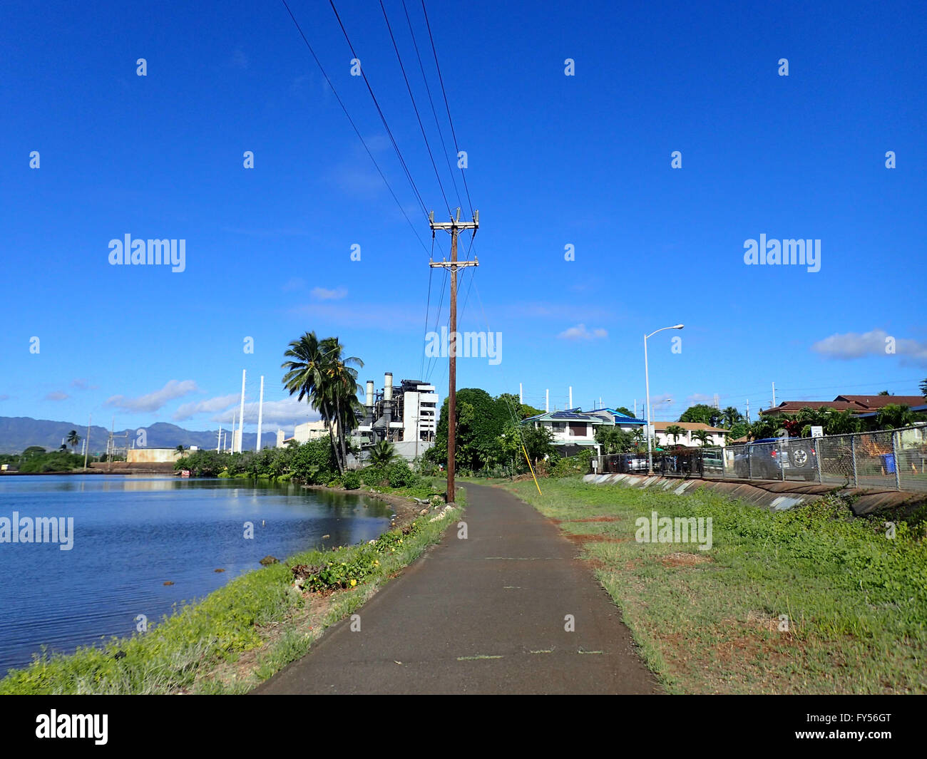 Pearl Harbor percorso in bicicletta lungo l'acqua con le linee elettriche aeree che portano alla pianta di potere a distanza su Oahu, Hawaii. Foto Stock