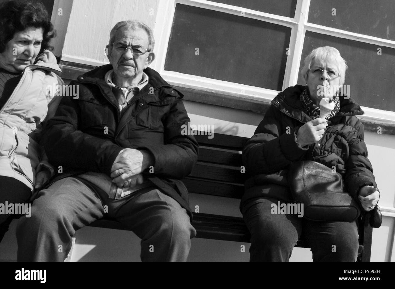 Una immagine in bianco e nero di persone seduta su una panchina in riva al mare. Uno è a mangiare il gelato Foto Stock