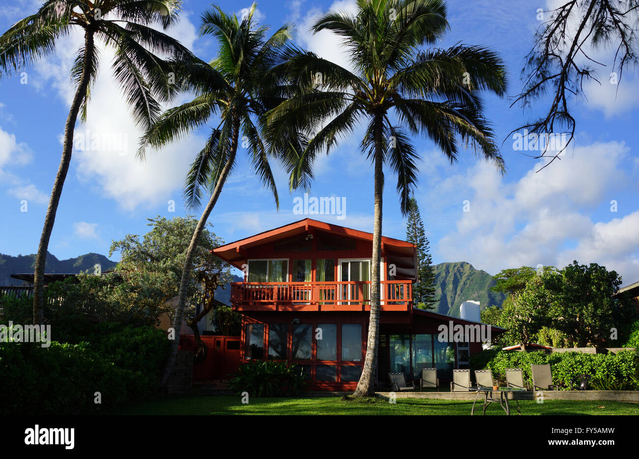 Rosso a Due Piani Casa sulla spiaggia con alte palme da cocco e le montagne sullo sfondo a Oahu, Hawaii su una bella giornata. Foto Stock