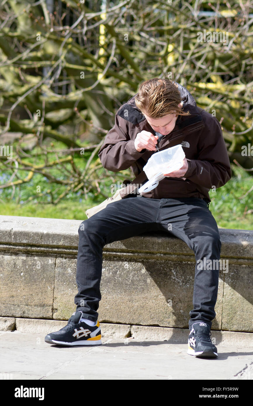 Giovane uomo seduto sulla parete di mangiare pasti da asporto al di fuori il Corpus Christi College di Cambridge, Cambridgeshire, Inghilterra Foto Stock