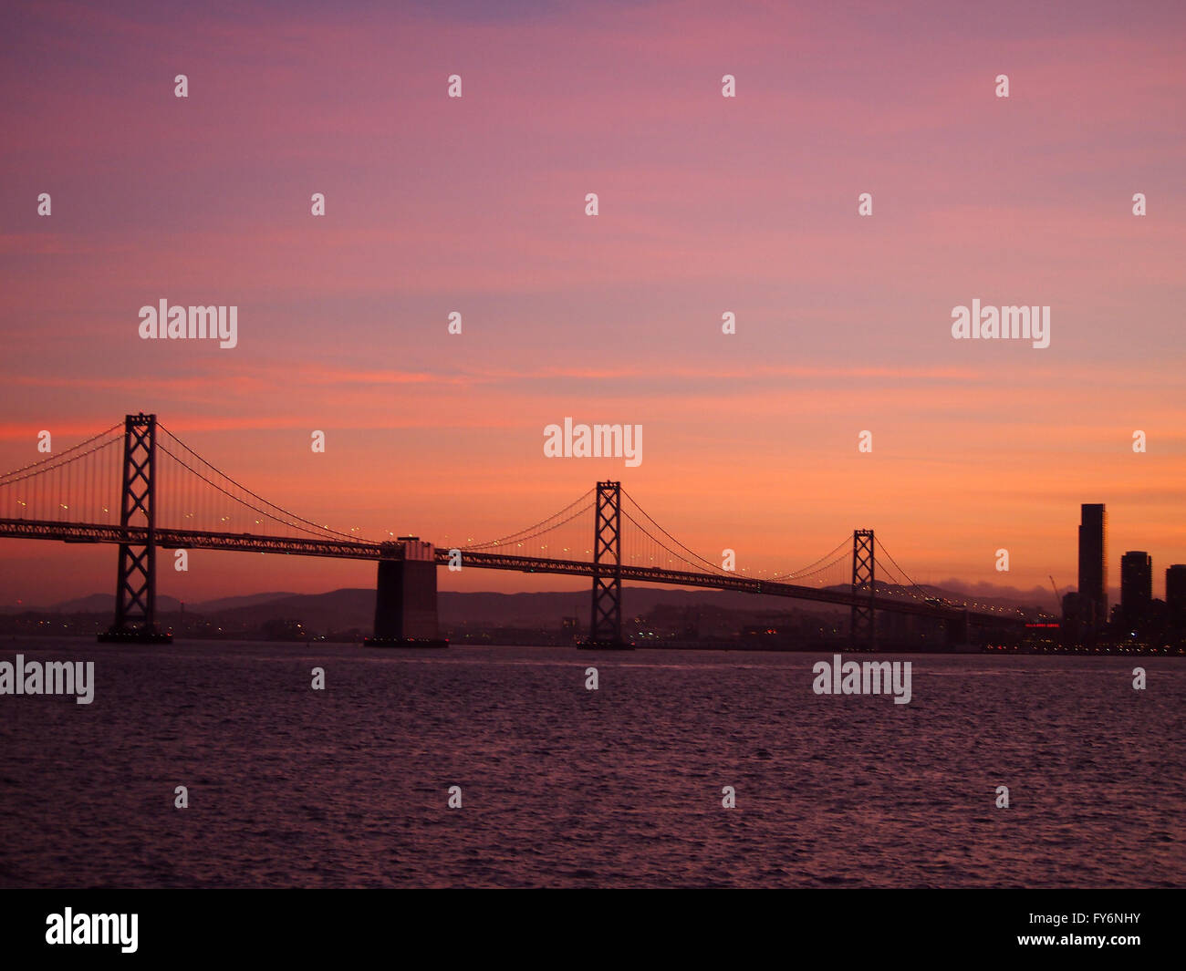 San Francisco lato del Bay Bridge e il centro cittadino di San Francisco al tramonto con il sorprendente rossi nel cielo visto dall'Isola del Tesoro. Foto Stock