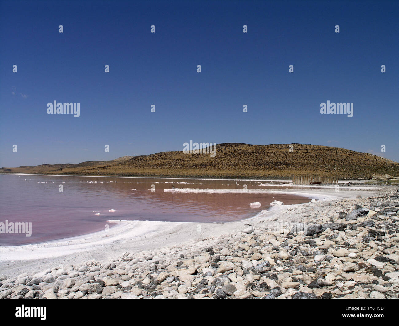 Il vecchio sito industriale lungo il salato a riva del grande lago salato con le montagne sullo sfondo. L'acqua si presenta di colore rosa a causa di una Foto Stock