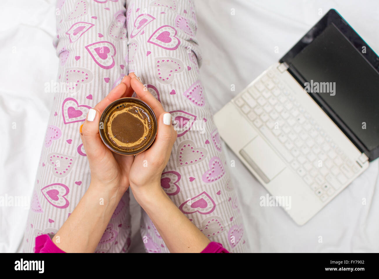 Donna con una tazza di caffè nel letto con un notebook Foto Stock