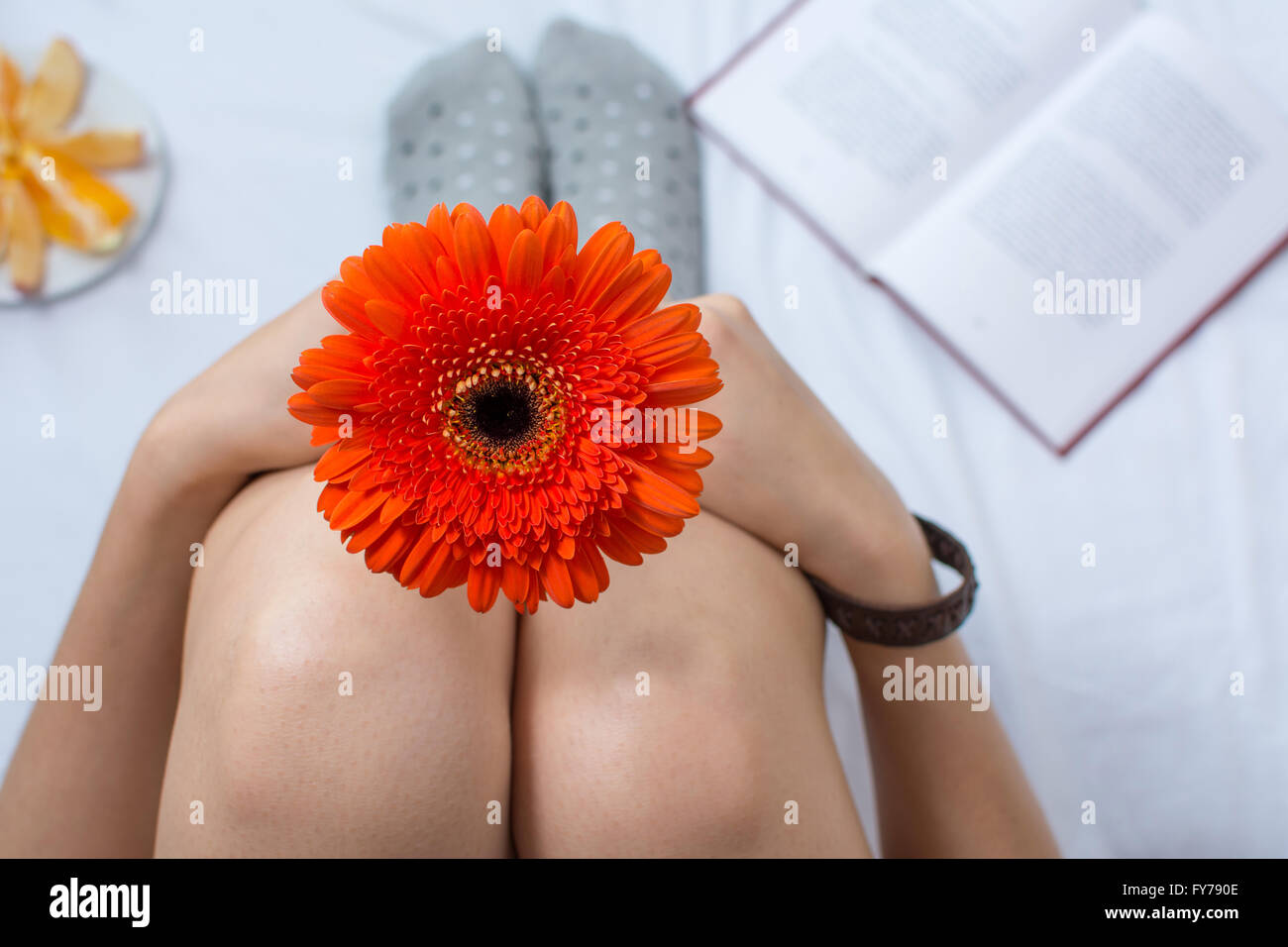 Donna che mantiene un orange gerbera fiore a letto Foto Stock