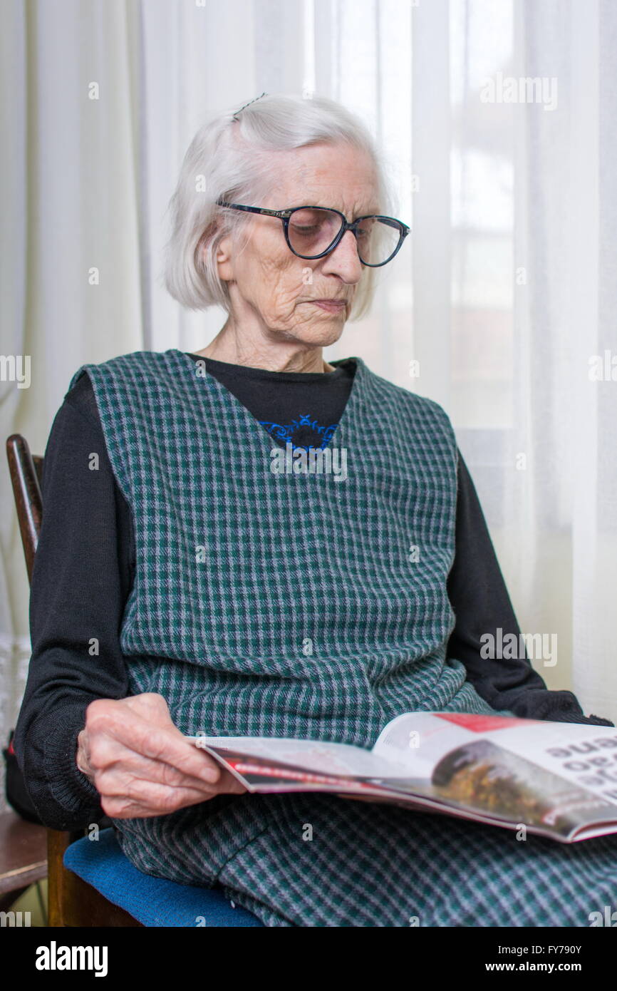 Novanta anni signora lettura quotidiani in ambienti interni Foto Stock