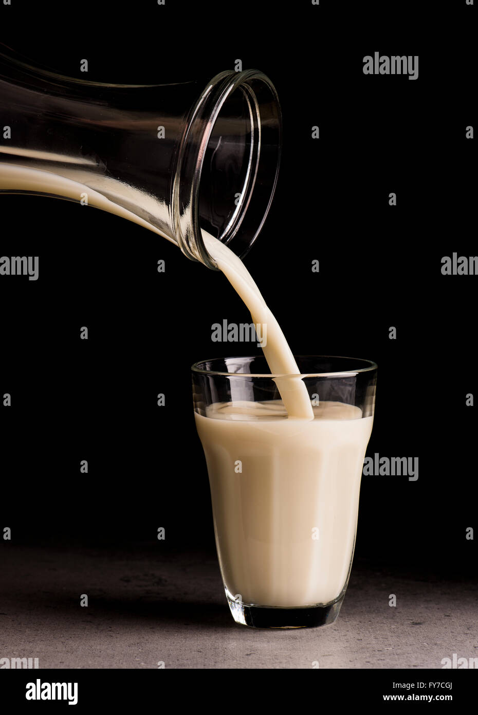 Latte di avena essendo versata da una bottiglia in un bicchiere. Sfondo nero. Foto Stock