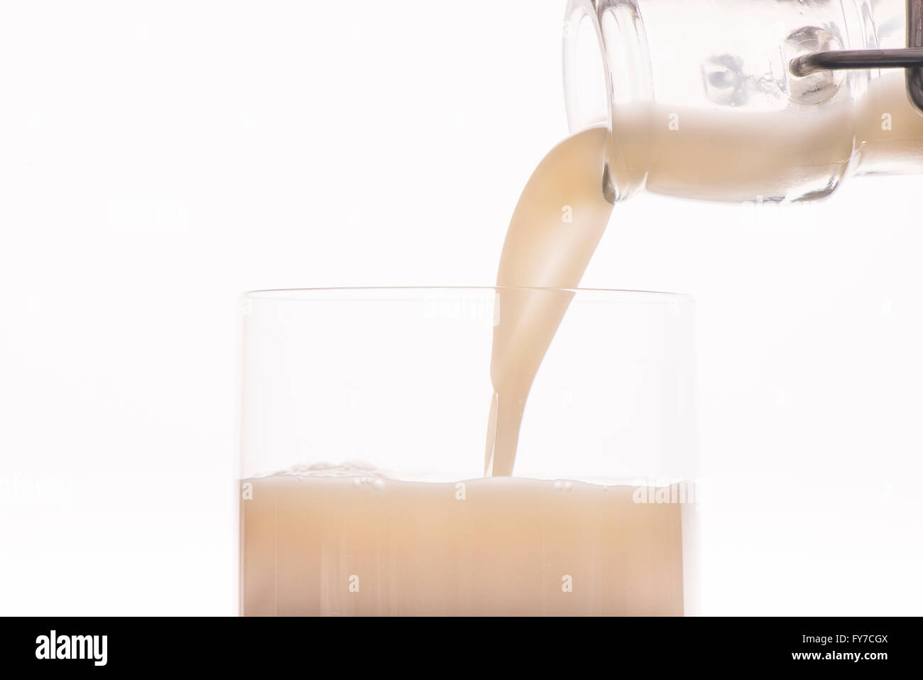Latte di avena essendo versata da una bottiglia in un bicchiere, vicino. Sfondo bianco. Foto Stock