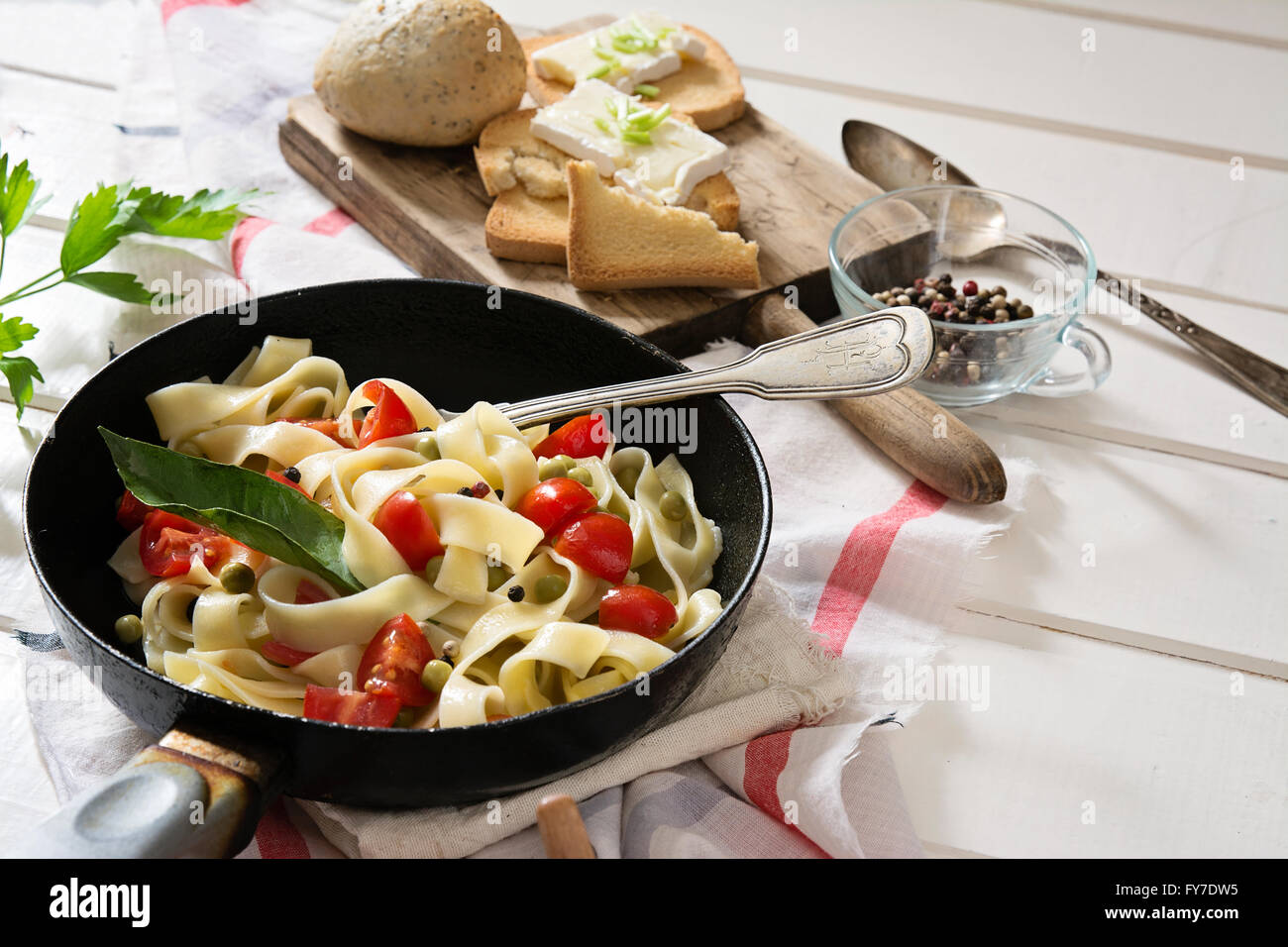 Tagliatelle con pomodorini in una padella, su bianco tavolo in legno e rosso tovaglia a scacchi Foto Stock