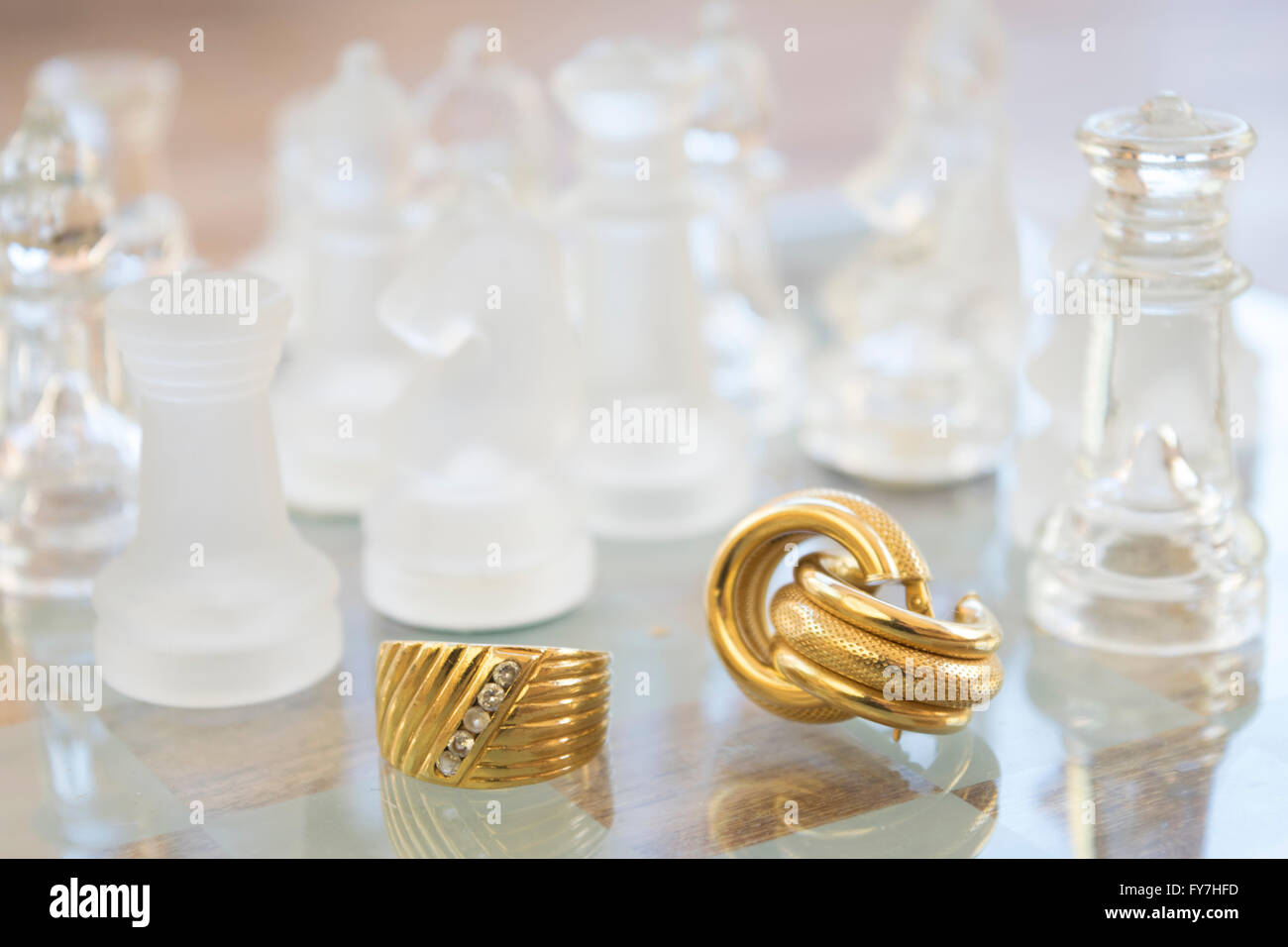 Famiglia Anello oro e orecchini su una scacchiera di vetro Foto Stock