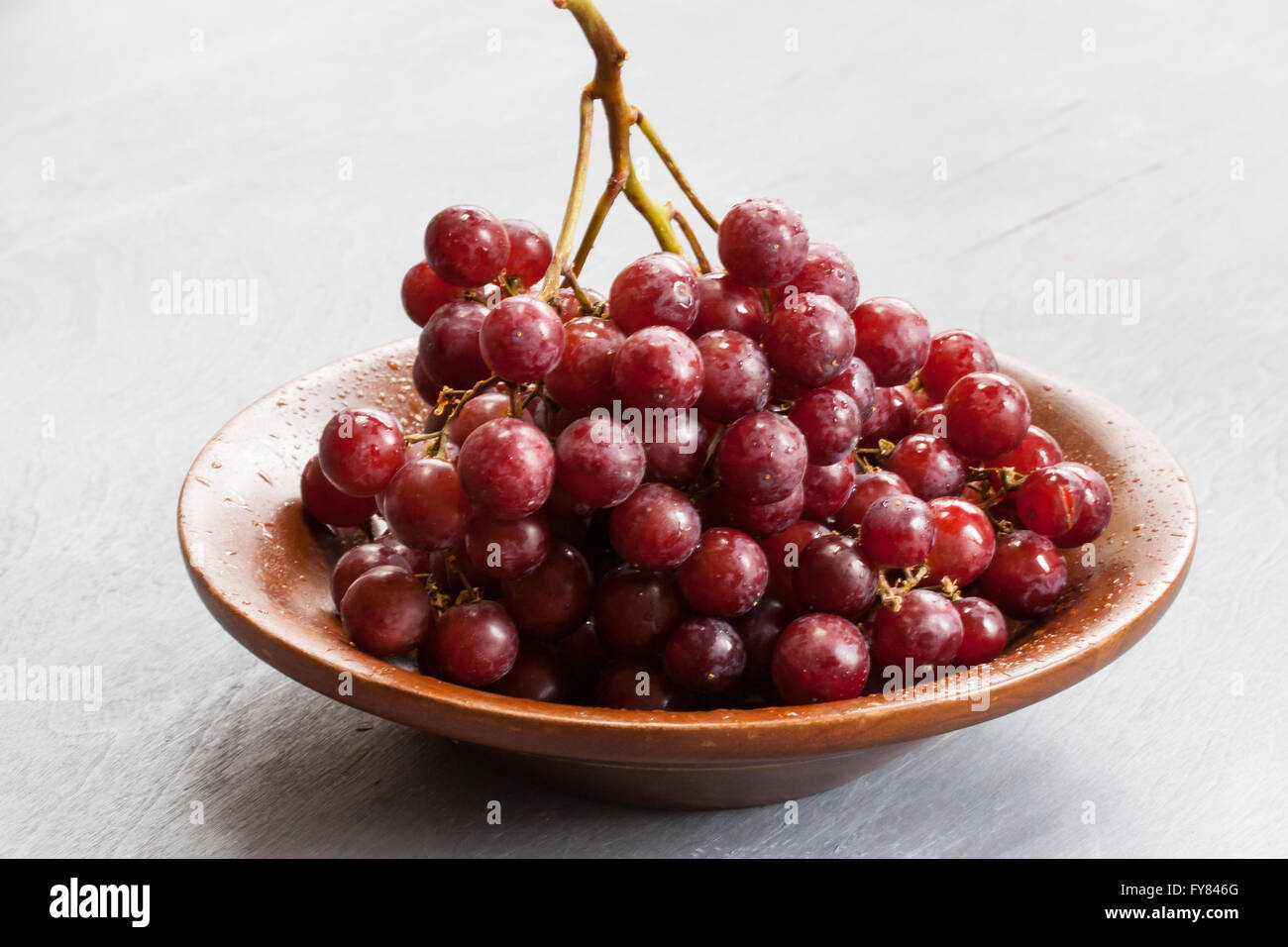 Rosso uva da tavola su una tavola di legno dai toni- piatto di frutta fresca close up fresca uva rossa su una piastra laterale per motivi indietro Foto Stock