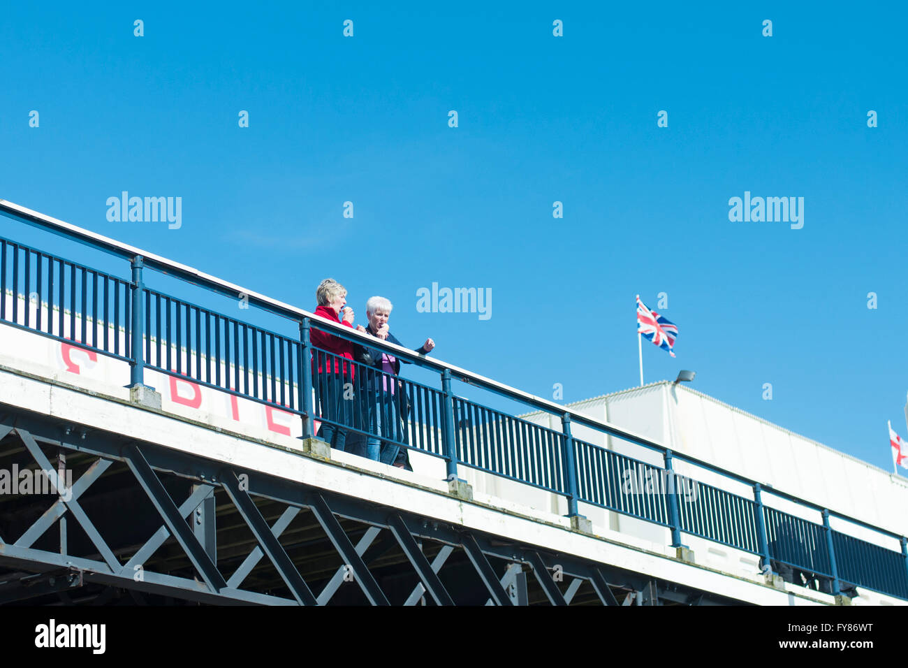 2 pensionati mangiare gelato sul molo a Southport con union jack flag in background Foto Stock