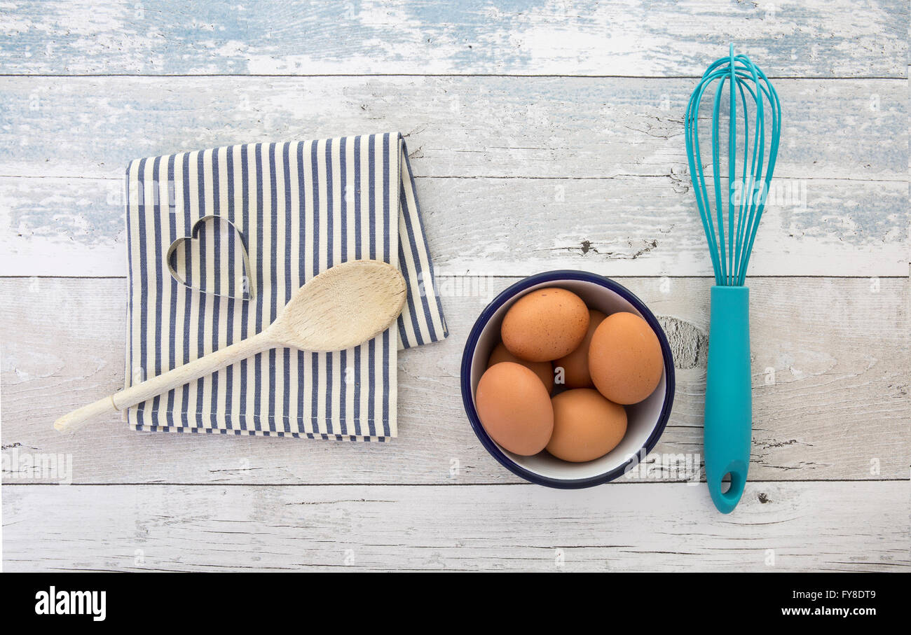 Le uova in una terrina con una frusta il cucchiaio di legno e tovagliolo su una tavola in legno rustico top shot dal di sopra Foto Stock