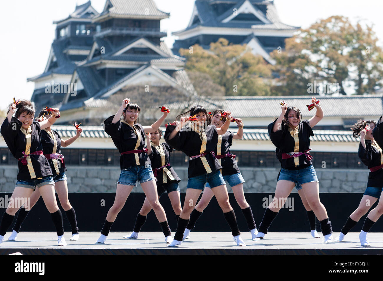 Femmina giapponese dance troupe di ragazze adolescenti, tenendo naruko, ballando sul palco all'aperto con castello di Kumamoto dietro di loro, durante il festival di Yosakoi. Foto Stock