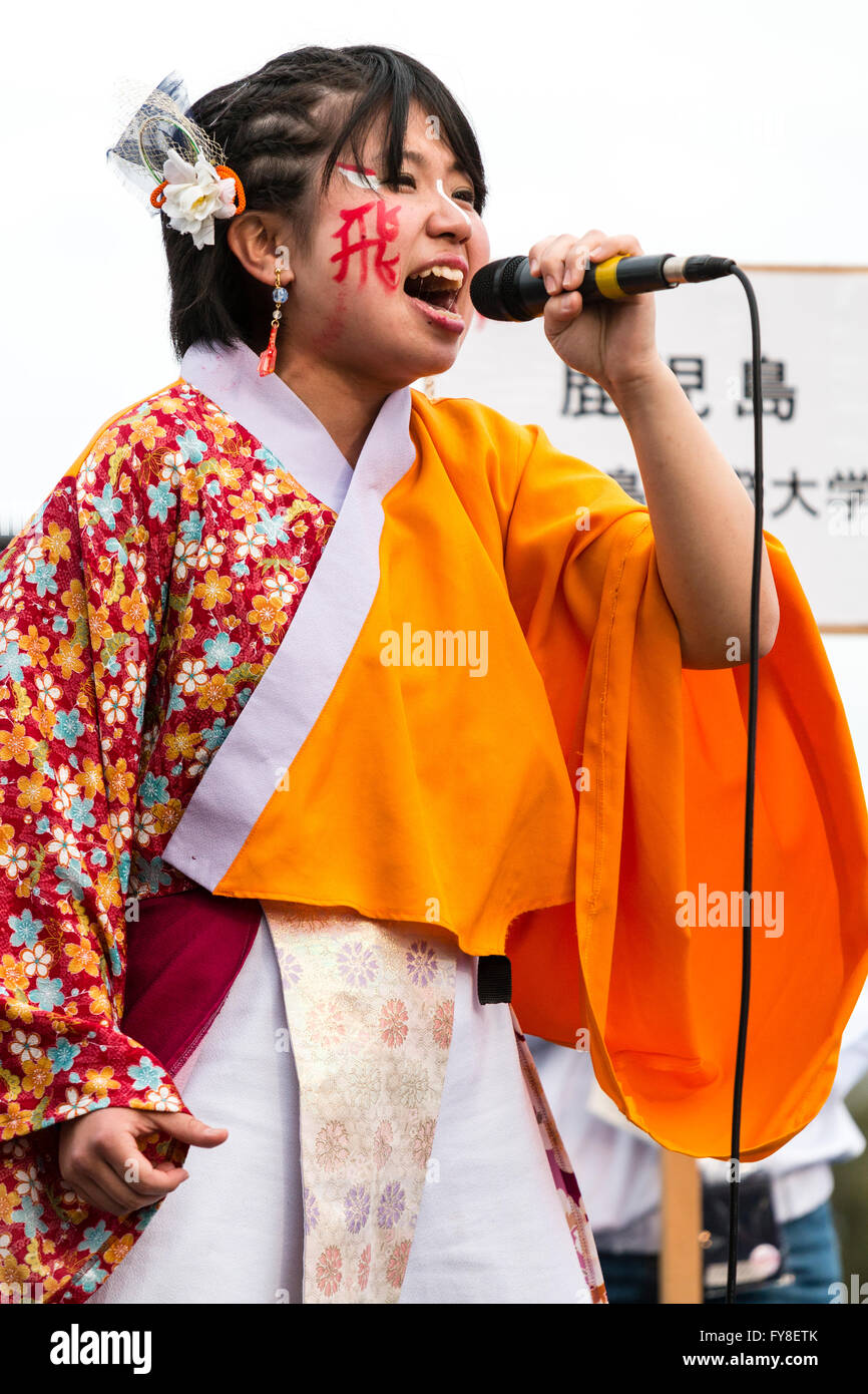 Ravvicinata di una giovane e bella donna giapponese annunciatore, in arancione yukata camicia, parlando nel microfono portatile a Yosakoi dance festival di Kumamoto. Foto Stock