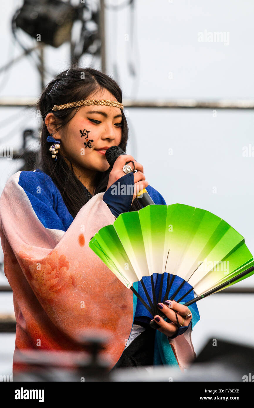 Ravvicinata di una giovane e bella donna giapponese annunciatore parlando nel microfono portatile e tenendo aperta la ventola a Yosakoi dance festival di Kumamoto. Foto Stock