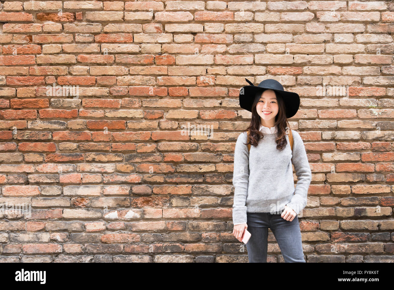 Bella ragazza asiatica in abiti alla moda, in piedi di fronte a mattoni rossi di sfondo a parete con spazio di copia Foto Stock