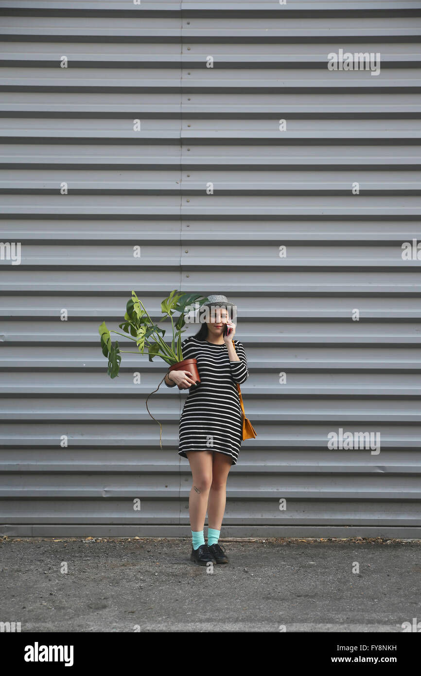 Donna di telefonare con lo smartphone che porta una Monstera deliciosa Foto Stock
