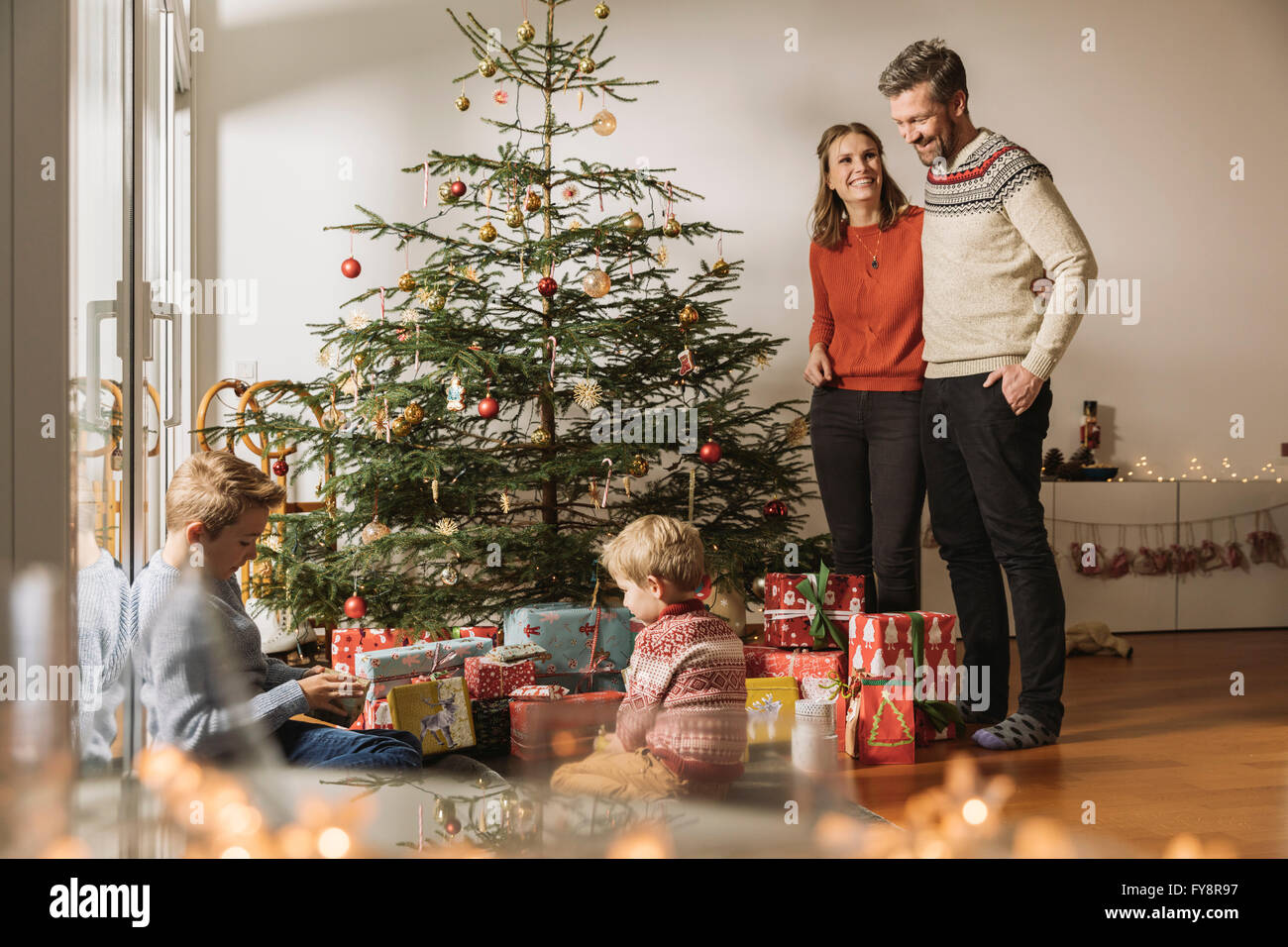 Genitori felici a guardare i loro figli scartare i regali di Natale Foto Stock