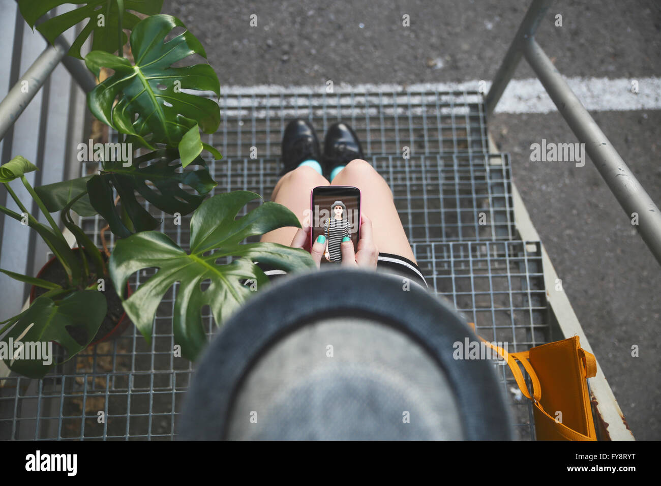 Vista superiore della donna seduta su scale azienda smartphone con la propria fotografia Foto Stock