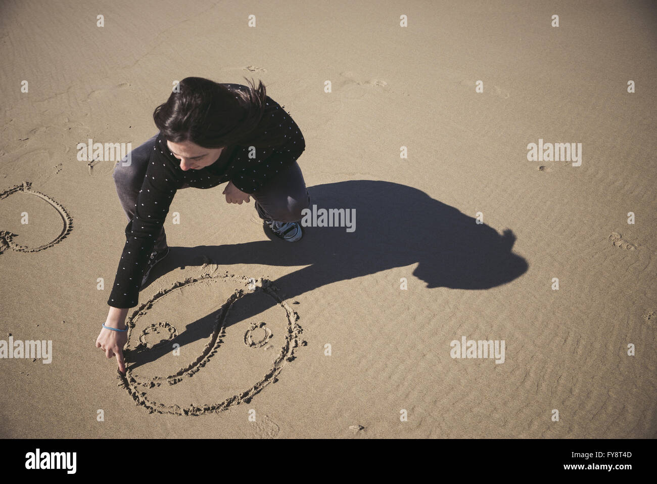 Donna di graffiare Yin Yang simbolo nella sabbia di una spiaggia Foto Stock