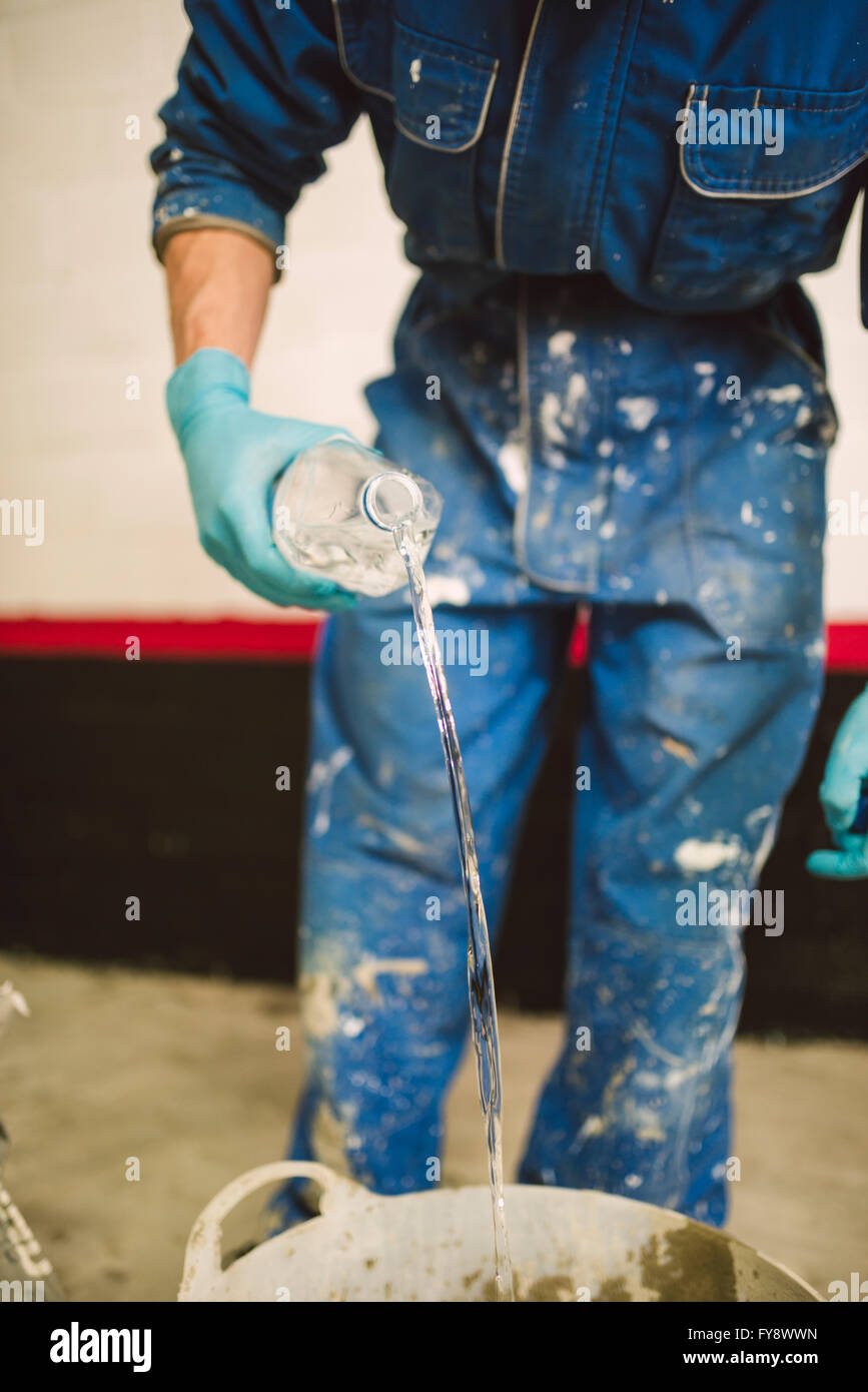 Muratore in preparazione di cemento nel secchio, versando acqua dalla bottiglia Foto Stock