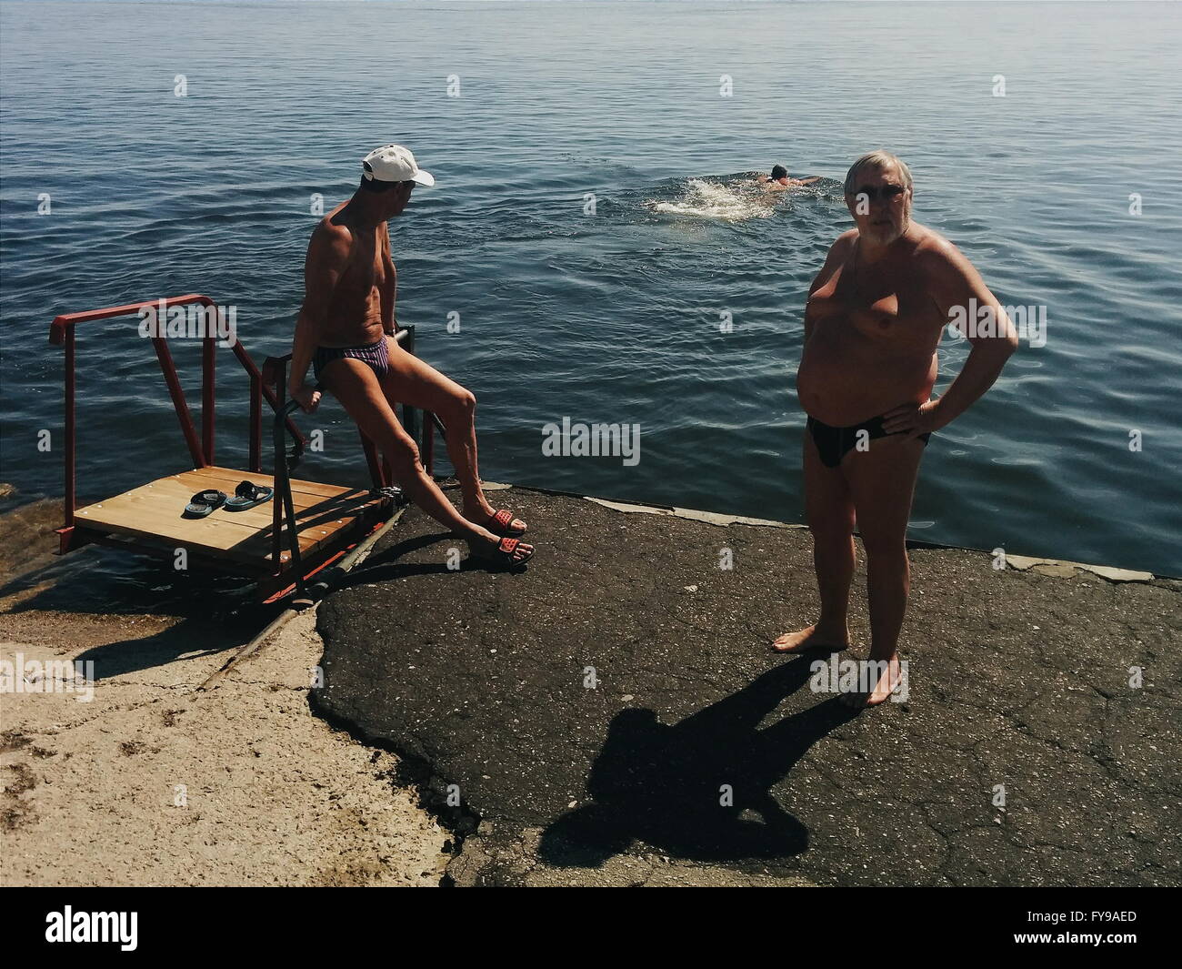 Saratov. 24 apr, 2016. Gli uomini appoggiano sul greto del fiume come il loro amico prende un bagno in Volga a Saratov, Russia, su apr. 24. 2016. Credito: Evgeny Sinitsyn/Xinhua/Alamy Live News Foto Stock