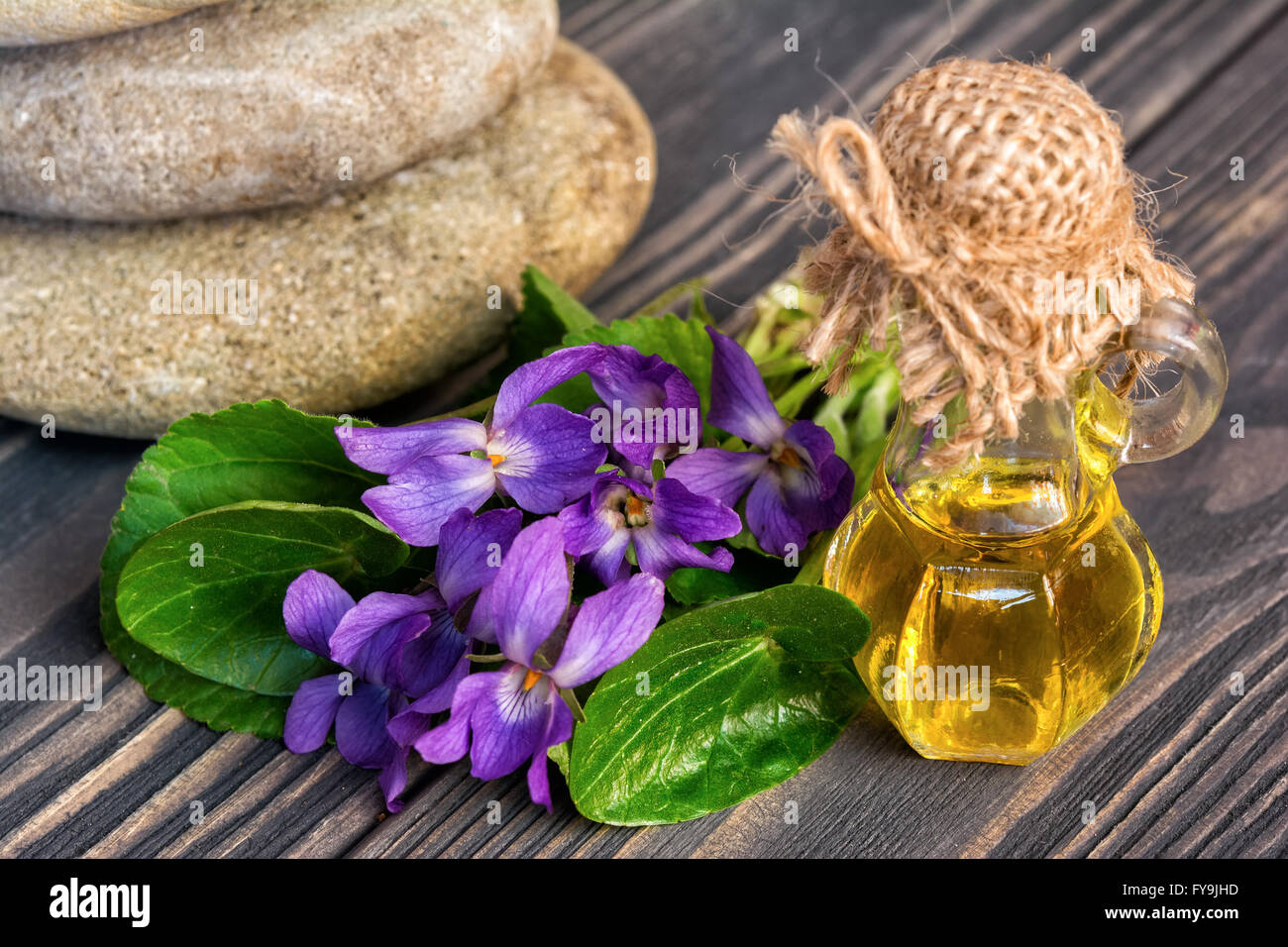 Olio e fiore di violette, zen pietre su sfondo di legno Foto Stock