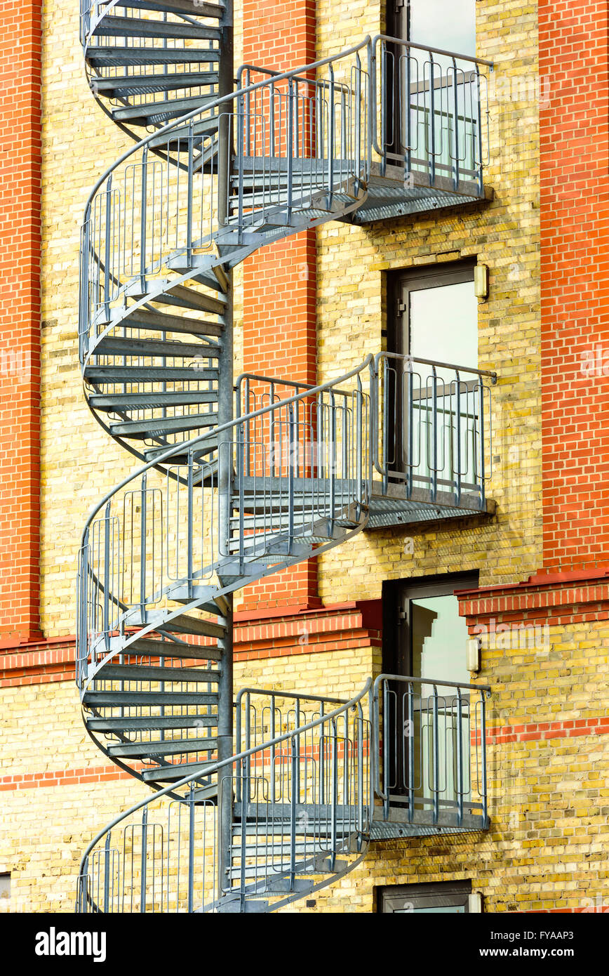 Scale a spirale che va dal pavimento al piano al di fuori di un giallo e rosso mattone nella costruzione. Vetro di emergenza porte che conducono ai passi sono clos Foto Stock