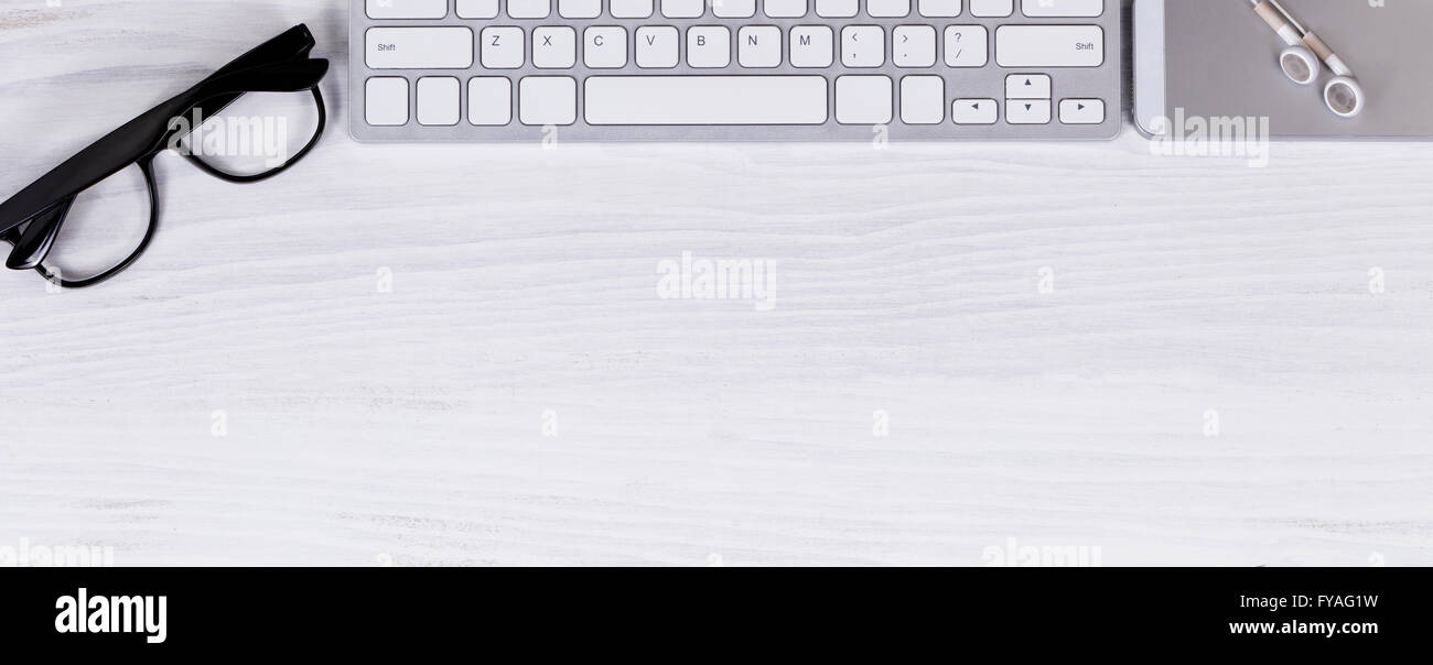 Vista aerea del desktop bianco con parziale della tastiera del computer, telefono cellulare, gli occhiali da lettura e auricolari. Foto Stock