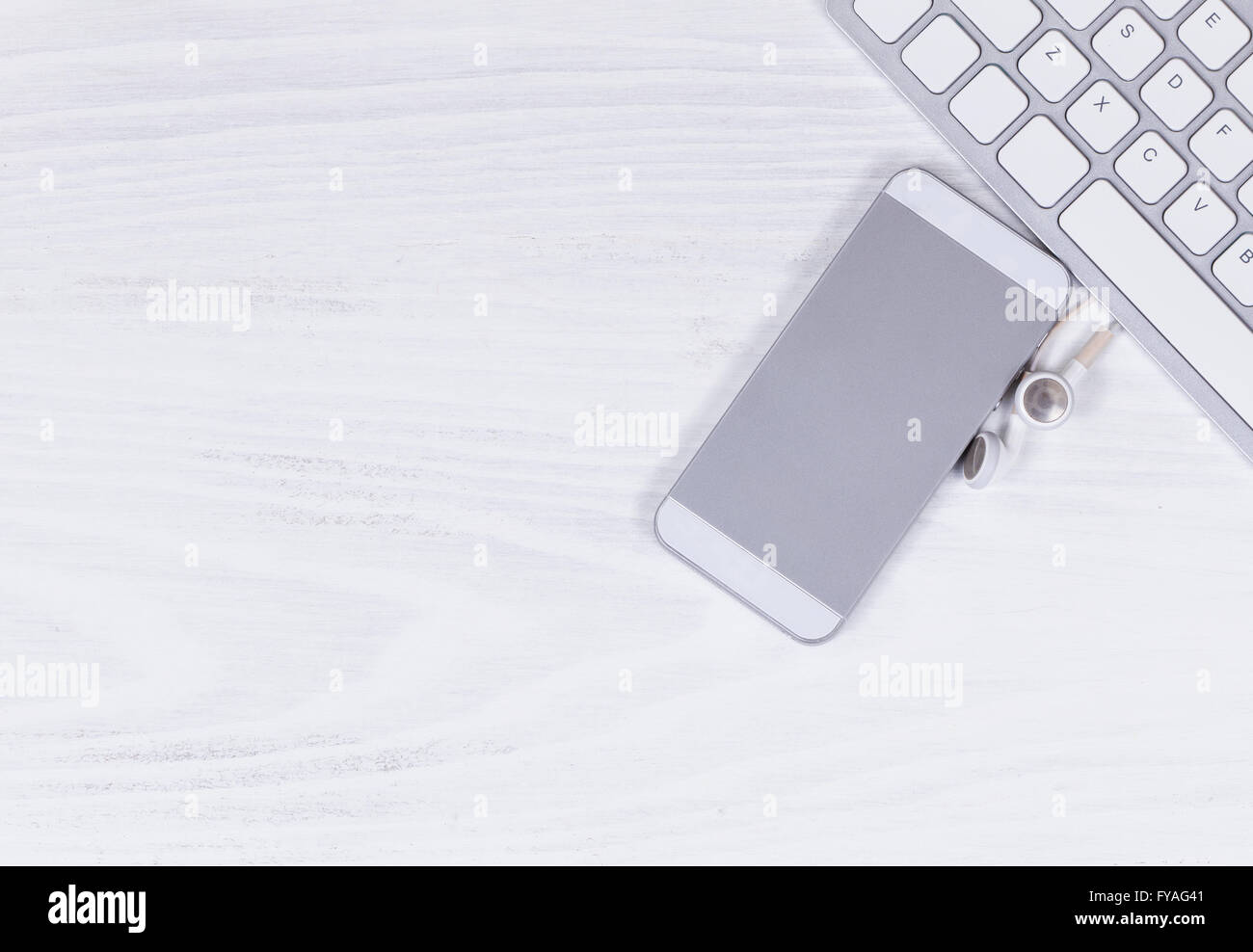 Vista aerea del desktop bianco con parziale della tastiera del computer, telefono cellulare e telefono all'orecchio. Foto Stock