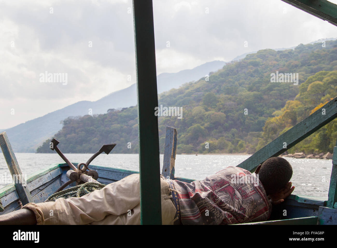 Irriconoscibile uomo africano di dormire sulla barca flottante contro di verdi colline e cielo nuvoloso lungo il lago Tanganica, Tanzania Foto Stock