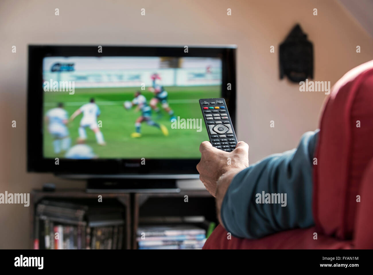 L uomo nella comoda poltrona la commutazione dei canali con telecomando per cercare gradevoli programma sul televisore nel soggiorno Foto Stock