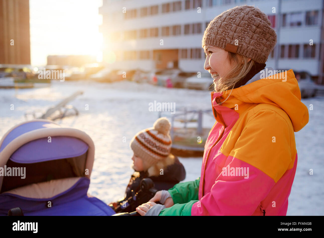 Giovane madre a piedi con baby bambino passeggino in inverno al tramonto. Foto Stock