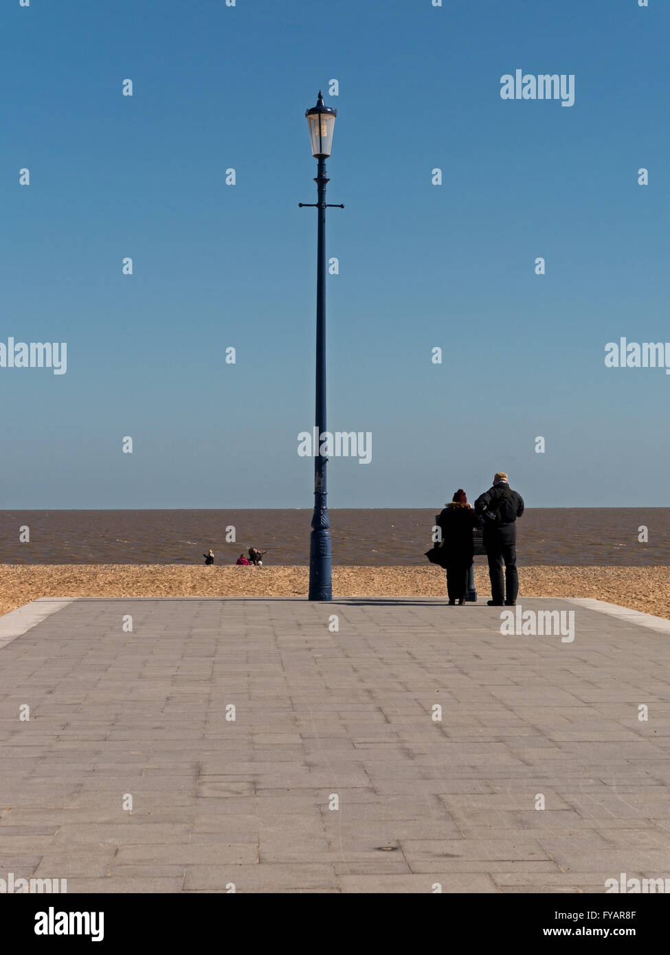 Giovane che guarda al mare da viale lastricato sulla spiaggia accanto a lampione, Great Yarmouth, Norfolk, Inghilterra Foto Stock