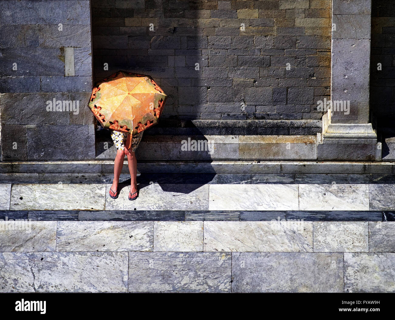 Una immagine da sopra guardando verso il basso su una donna prendendo rifugio dal caldo in estate sotto un ombrello coloratissimo a Pisa, Italia. Foto Stock