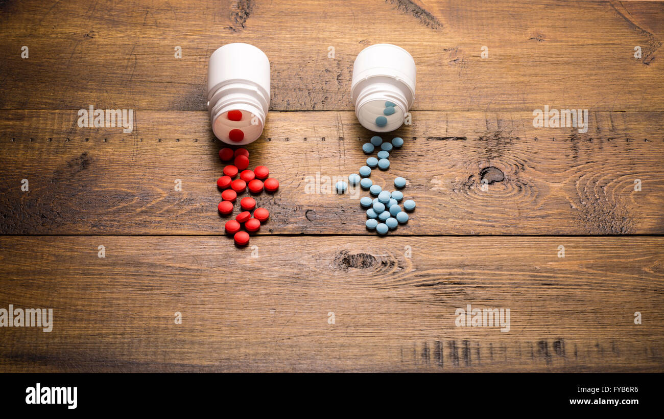Diffusa dal medical bottiglia di rosso e di blu pillole su sfondo di legno Foto Stock