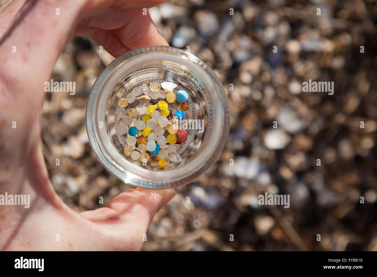 Una mano che regge un vaso di vetro con piccolo di plastica nurdles trovato su una spiaggia scozzese. Foto Stock
