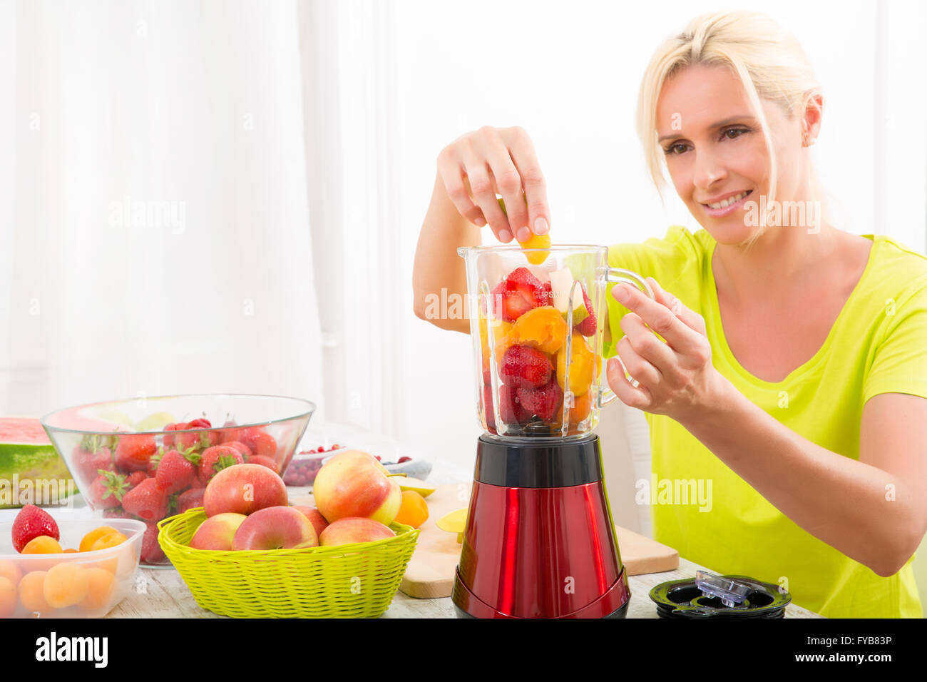 Una bella donna matura preparare un frullato o succo di frutta in cucina. Foto Stock
