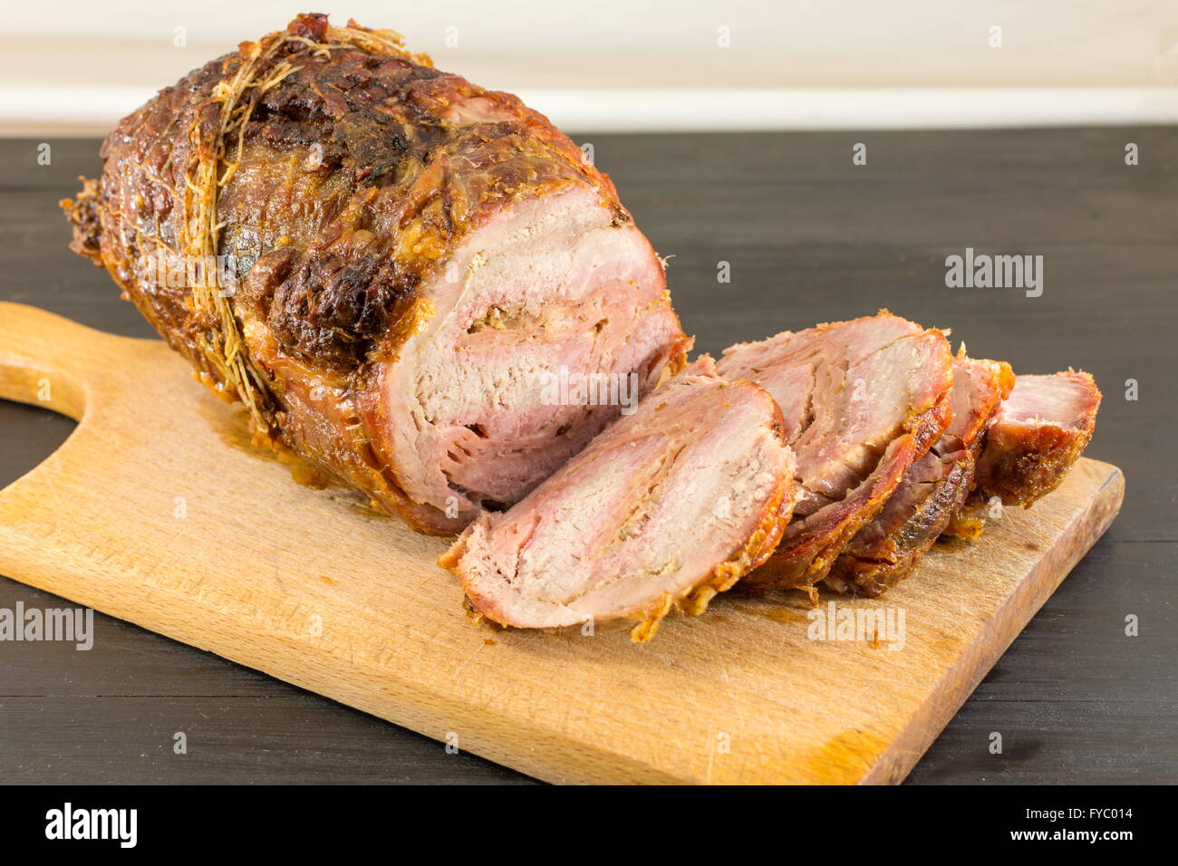 Arrosto di maiale arrotolata la carne su un tagliere su una tavola nera Foto Stock