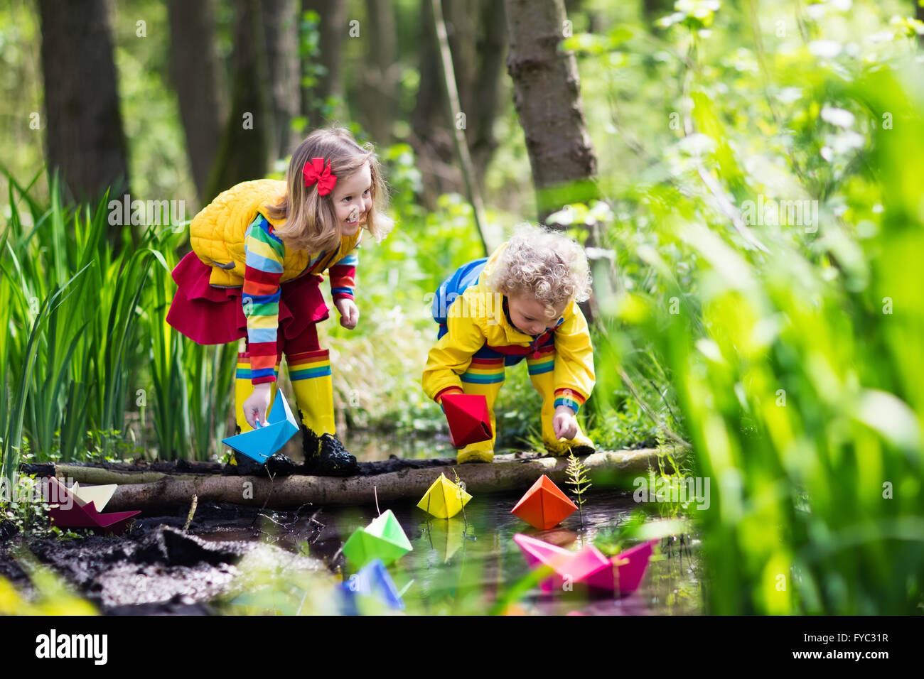 I bambini giocano con coloratissime barche di carta in un piccolo fiume su una soleggiata giornata di primavera. Ragazzi che giocano a esplorare la natura. Foto Stock