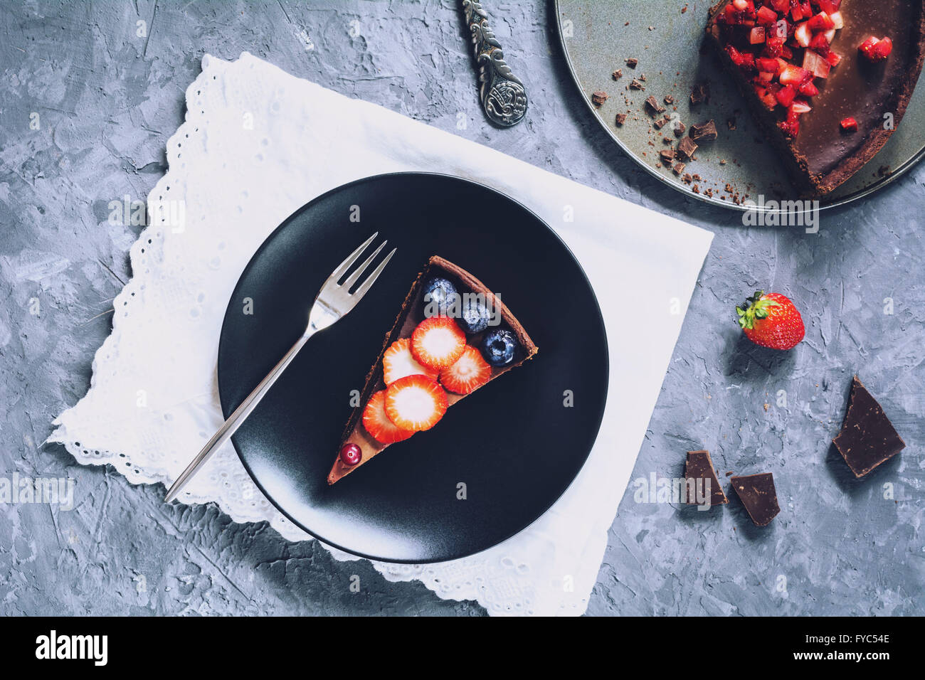 Fetta di mousse al cioccolato tart (torta) e rabboccato con fragole, mirtilli e mirtilli rossi sulla piastra nera. Tabella vista superiore Foto Stock