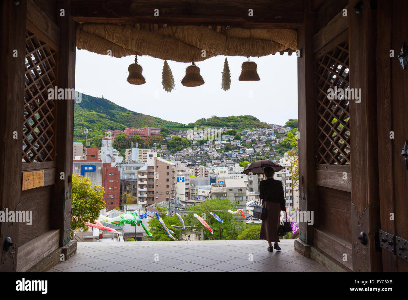 Donna con un ombrellone a piedi attraverso l'arco d'ingresso del Suwa Santuario a Nagasaki, in Giappone con con una vista della città Foto Stock