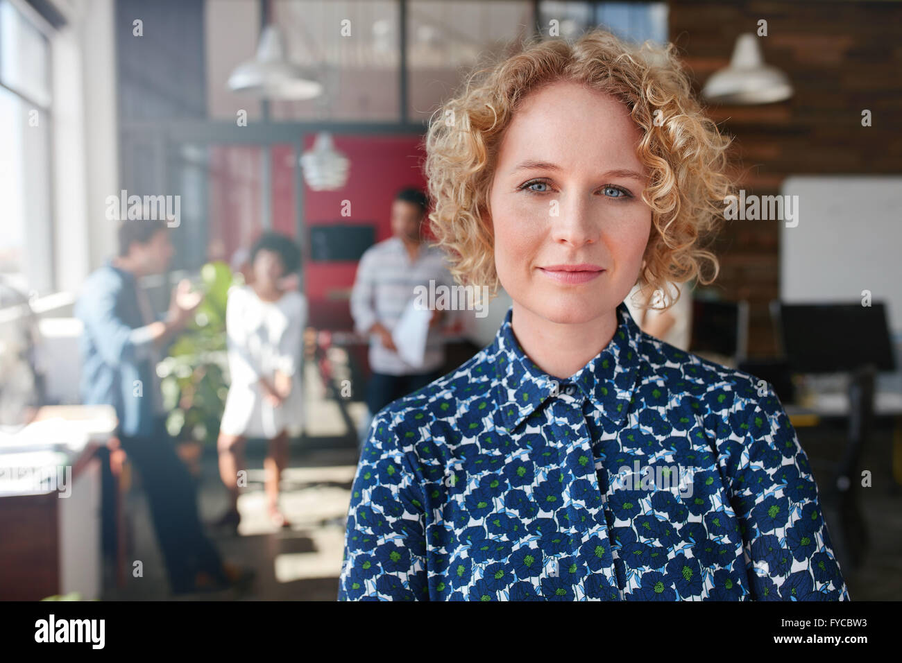 Ritratto di una giovane e bella donna designer in ufficio con alcuni colleghi per discutere in background. Foto Stock