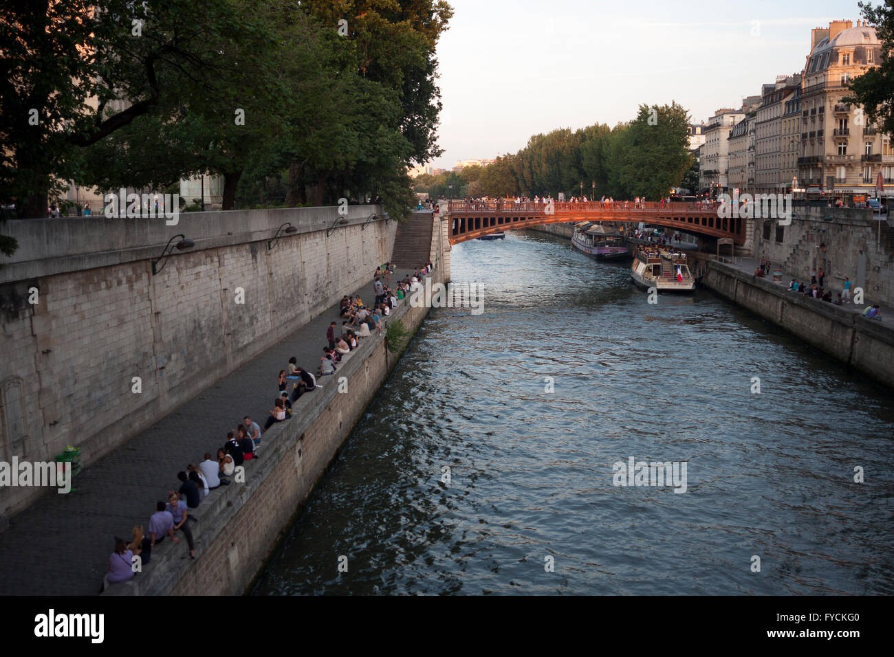 I membri del pubblico godendo del tramonto accanto al canale quando una barca di passare sotto il ponte a Parigi. La Francia. Pic pak@ Mera Foto Stock