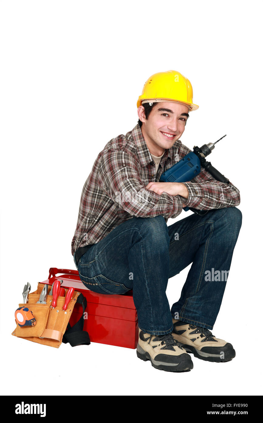 Giovane artigiano tenendo un trapano e seduto su una cassetta portautensili Foto Stock
