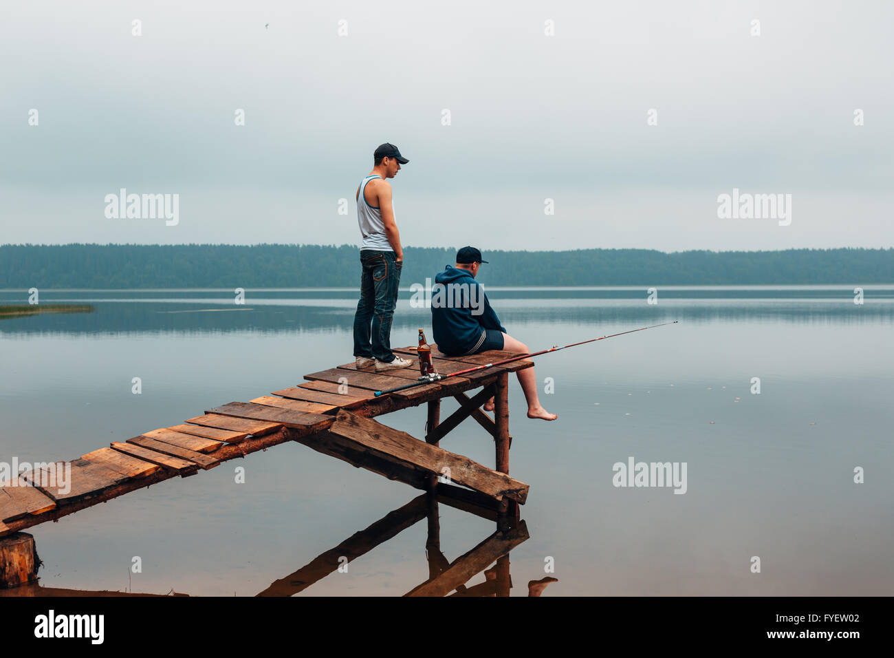 Due uomini sono in attesa su un ponte di legno quando i pesci sono di mordere. Foto Stock