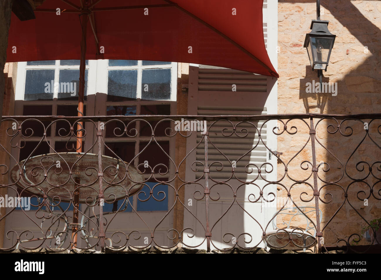 Ombrellone rosso e arrugginendo metallo tavolo e sedia sul balcone della casa francese nel vicolo laterale nella regione della Dordogne della Francia Foto Stock